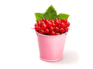 Ripe red currants with green leaves in a pink bucket on a white background. Close-up. Still life.