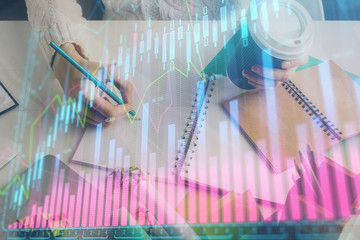 Financial forex graph displayed on hands taking notes background. Concept of research. Multi exposure