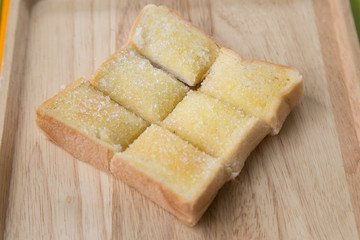 Toasted bread with butter and sugar in wooden tray with table background