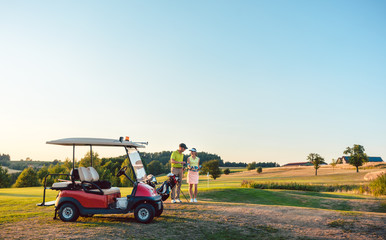 Woman and her partner or instructor holding various golf clubs near golf cart