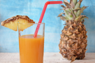 Pineapple cocktail or juice in glass bottles with straws with ice and pineapples on a blue or pink background
