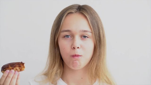 Unhealthy eating concept. Beautiful young woman with long blond hair eating eclair cake and looking at the camera