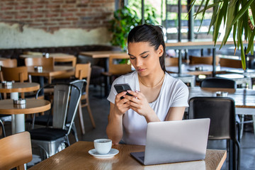 Young woman with coffee cup and laptop talking on her smart phone. Woman taking a break. Doing Business From the coffee shop