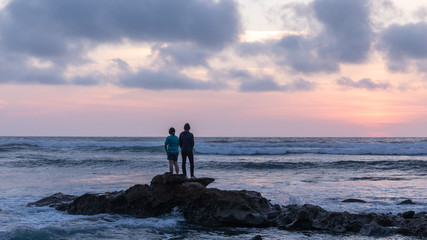 Asian young man and woman standing on a rock watching sunset at Sunset Cliffs Natural Park, San Diego, California