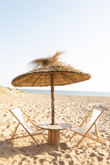 table et chaises longues sous parasol en paille sur la plage devant le front de mer