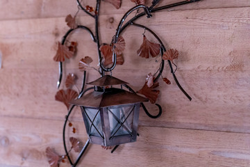 A vintage metal lantern hanging on a metal stem decorated with leaves on a wooden wall in a house