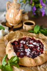 Open strawberry pie with mint leaves on a brown background with coffee and flowers in a rustic style
