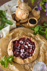 Open strawberry pie with mint leaves on a brown background with coffee and flowers in a rustic style