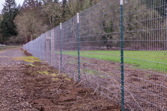 A welded wire mesh fence on a border of a farm along a gravel walkway