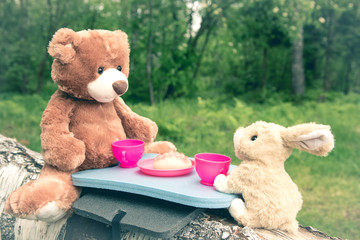 True friends - the rabbit and the little bear are sitting on the grass during a picnic in a park,