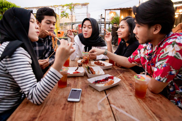 Group of young friends enjoying meal in outdoor cafe on the building rooftop