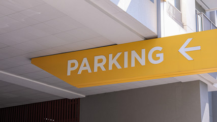Custom parking sign with white letters and an arrow pointing to the left under a ceiling of a parking garage