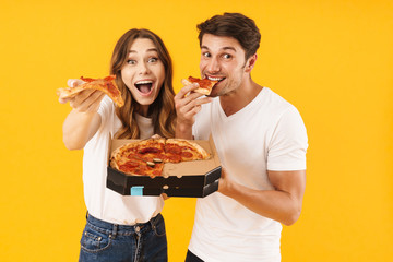 Portrait of attractive couple man and woman in basic t-shirts smiling while eating pizza from box
