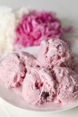 Balls of berry ice cream on a plate and white and pink peonies on a white background side view, copy space