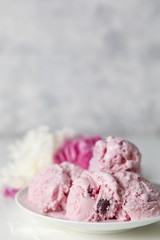 Balls of berry ice cream on a plate and white and pink peonies on a white background side view, copy space