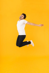 Fototapeta na wymiar Full length photo of beautiful man in basic t-shirt rejoicing and jumping with spreading arms aside
