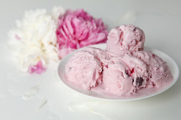 Balls of berry ice cream on a plate and white and pink peonies on a white background side view
