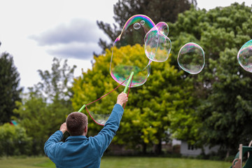 A man in blue fleece jacket making giant soap bubbles with two green wands and a rope