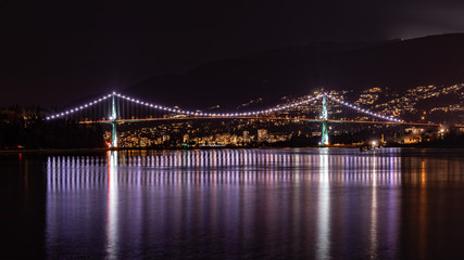 Night panorama of Lions Gate bridge connecting Stanley Park with North Vancouver, BC, Canada. Bridge lights reflecting on a silky water of Vancouver Harbor.