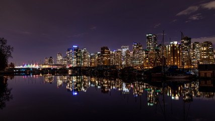 Naklejka na ściany i meble Vancouver, BC \ Canada - 13 March 2019: A night long exposure photo of marina inside Burrard Inlet of Vancouver Harbor with many yachts and boats against colorful illuminated city skyline