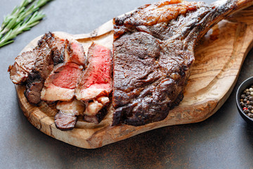 Grilled dry-aged marble beef steak Tomahawk on black wooden board with spices.