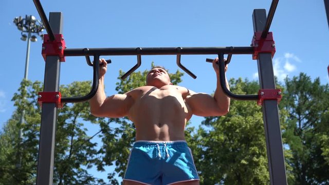 young man doing exercise on the crossbar during the morning workout outdoors. Athletic muscular athlete with a naked torso.