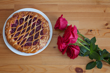 Red roses and berry pie on the wooden table, top view