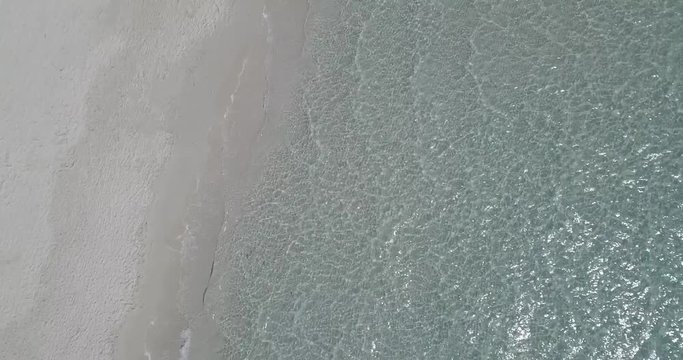 AERIAL 4K Shoreline of a beautiful white sand beach with small water ripples breaking with light reflections