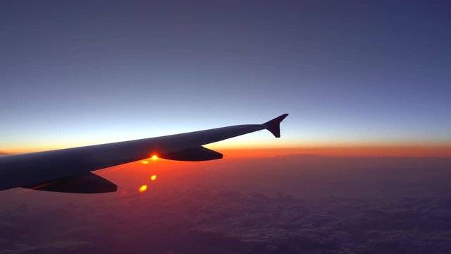 Up in the air, view of aircraft wing silhouette with dark blue sky horizon and cloud background in sun rise time, viewed from airplane window