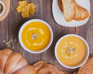 Two bowls of delecious homemade pumpkin soup with cream on the wooden table top view
