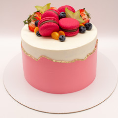Delicate white-pink cake decorated with macaroons, strawberries, blueberries and carambola. On a white background.