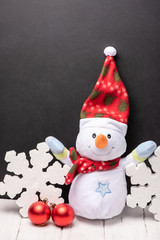Cheerful snowman toy in a red hat and scarf with foam  snowflakes on the background of black chalk board