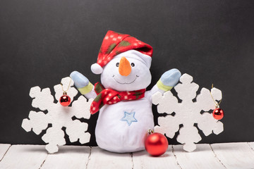 Cheerful snowman toy in a red hat and scarf with foam  snowflakes on the background of black chalk board