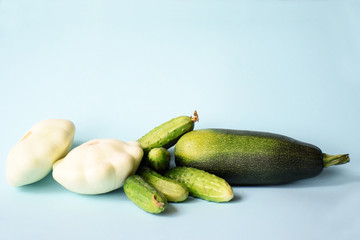 Summer green vegetables zucchini, cucumbers and white pattypan squash on a light blue background with space for text. Still-life of summer harvest. Vegetarians and kitchen concept.
