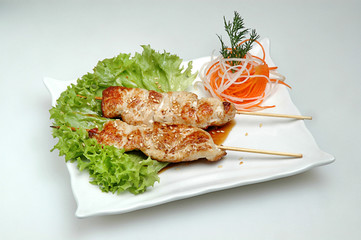 On a white square plate lies salad and on top a mini barbecue on a gray isolated background