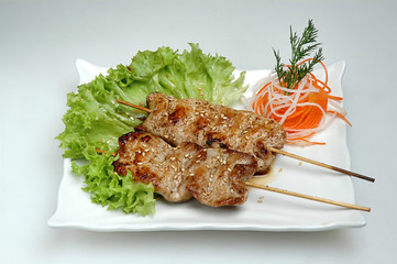 On a white square plate lies salad and on top a mini barbecue on a gray isolated background