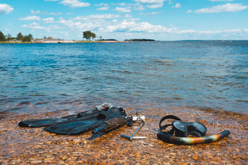 The equipment of the underwater hunter on the shore. Clear warm day by the sea. In the frame underwater mask with a tube, scuba gun and flippers