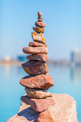 Red stone stack tower balance and horizontal blurred buildings and sea surface - symbol of succesful business build