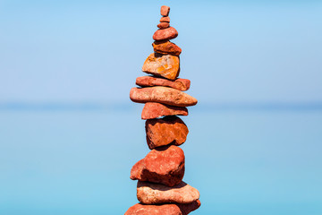 Fototapeta na wymiar Red stone stack tower balance and horizontal blurred sea surface