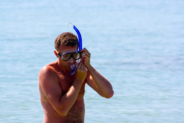 Portrait of man putting on the diving equipment with calm light blue sea water at the background.