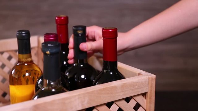 Woman taking bottle of wine from wooden crate on blurred background, closeup