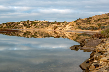 Fototapeta na wymiar The a calm onkaparinga river at southport with the sand dunes and the clouds reflecting on the water at port noarlunga south australia on 3rd July 2019
