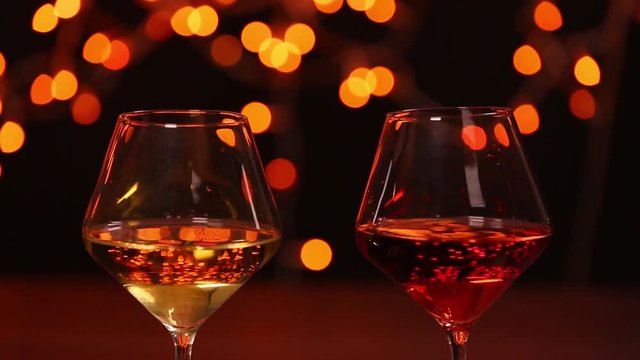 Couple clinking glasses with red and white wine against festive lights, closeup