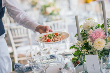 Assorted ham and sausage made from beef and pork cut into thin slices with olives and tomatoes for serving to guests, on a white plate in the hands of a waiter from a restaurant catering wedding event