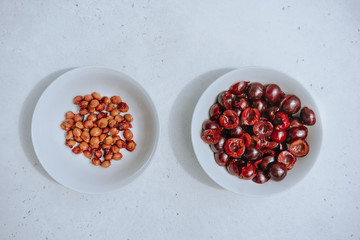 Halves of berries dark red cherries and separated bones in different white bowls on white background