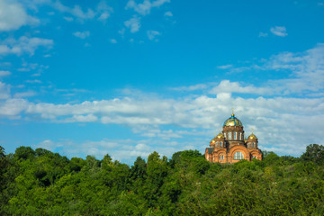 Orthodox church on a hill. Christian traditional temple on background of cloud blue sky and green forest trees at sunny summer day. Architecture and nature concept view