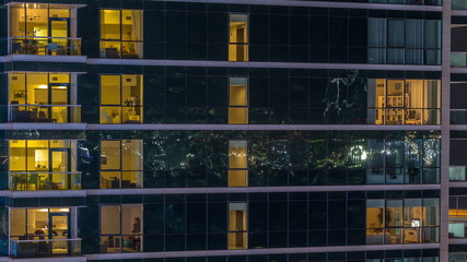 Fototapeta na wymiar Glowing apartment windows at night in glass skyscraper timelapse