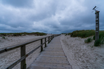 Fototapeta premium Holzsteg mit Sanddünen und Gewitterwolken