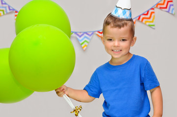 Fototapeta na wymiar A little boy smiles in a festive cap and holds three green balloons. Celebrates his birthday.