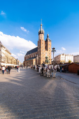 Fototapeta na wymiar Krakow, Poland - April, 2019: Two Horses In Old-fashioned Coach At Old Town Square In Cloudy Summer Day. St. Mary's Basilica Famous Landmark On Background. Church of Our Lady Assumed into Heaven.